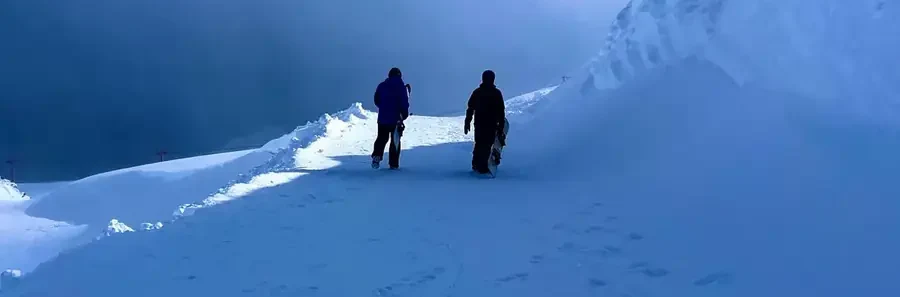 Duas pessoas caminhando na neve com pranchas de snowboard
